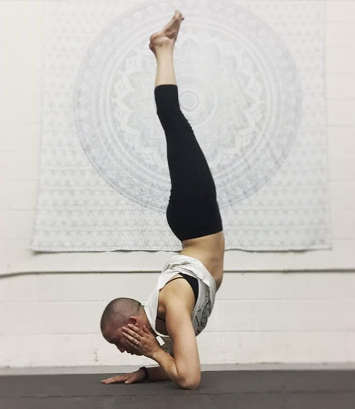 A bald woman performs an elbow stand in front of a white tapestry